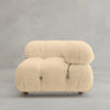 The Belmont Sofa Left Armrest features a modern modular design with soft, textured beige fabric, rounded edges, visible tufting, and exposed metal accents, shown against a plain gray background.