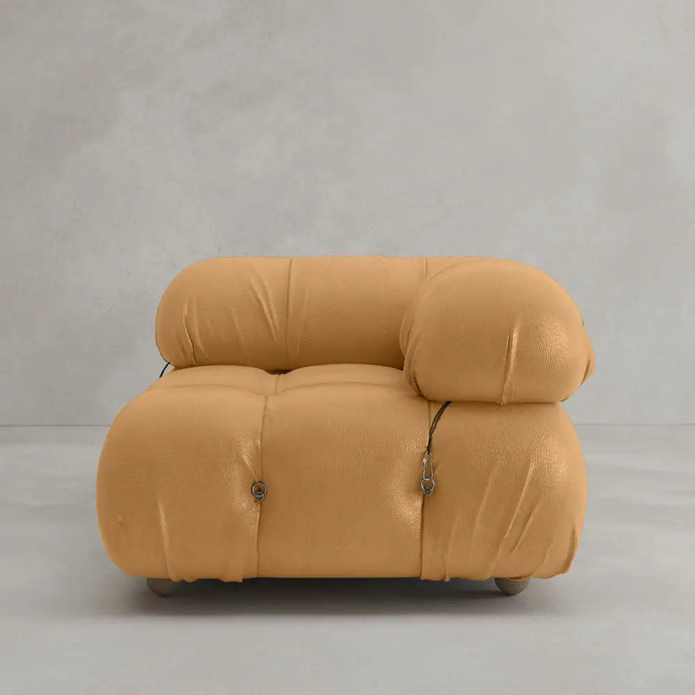 The Belmont Sofa Left Armrest features a modern tan design with plush, overstuffed cushions and visible black fastening cords, evoking a modular aesthetic against a plain light gray background.