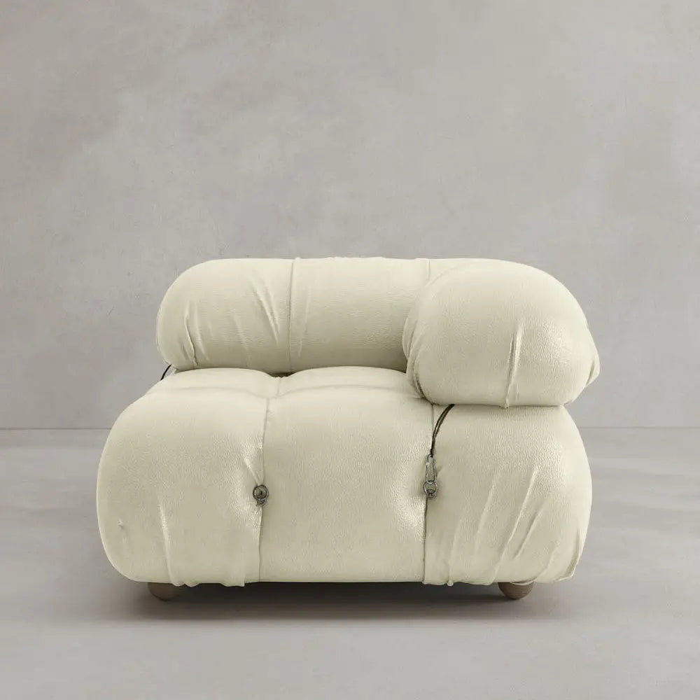 A modern, plush white Belmont Sofa Left Armrest with a rounded, tufted design and metal fasteners, featuring modular elements, set against a plain light gray wall and floor.