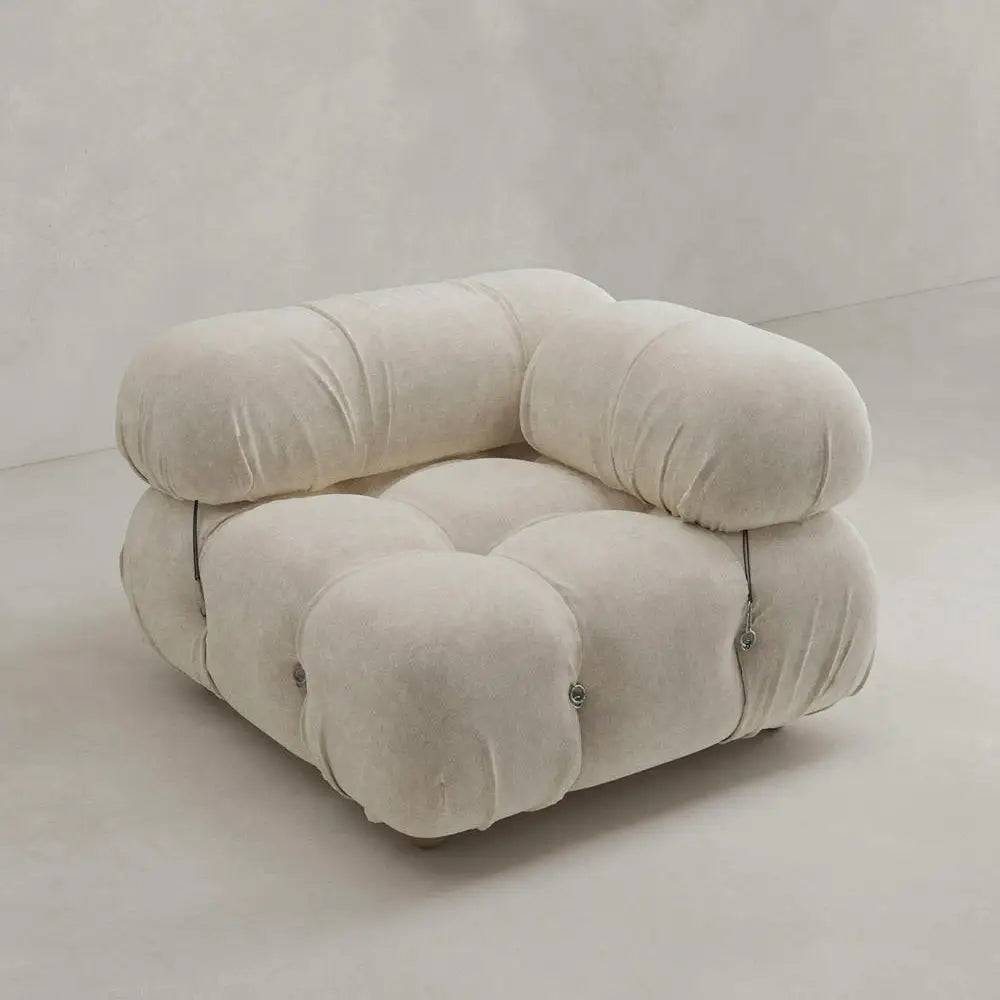 The Belmont Sofa Left Armrest features plush, overstuffed cushions in soft beige fabric with marshmallow-like curves and button accents, creating a modern look against a light, minimalist background.