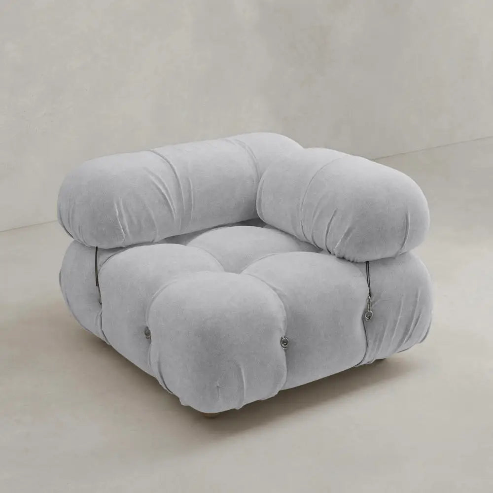 The Belmont Sofa Left Armrest features plush, tufted light gray upholstery with soft, rounded edges and marshmallow-like curves, set on a neutral-toned floor against a plain beige wall.