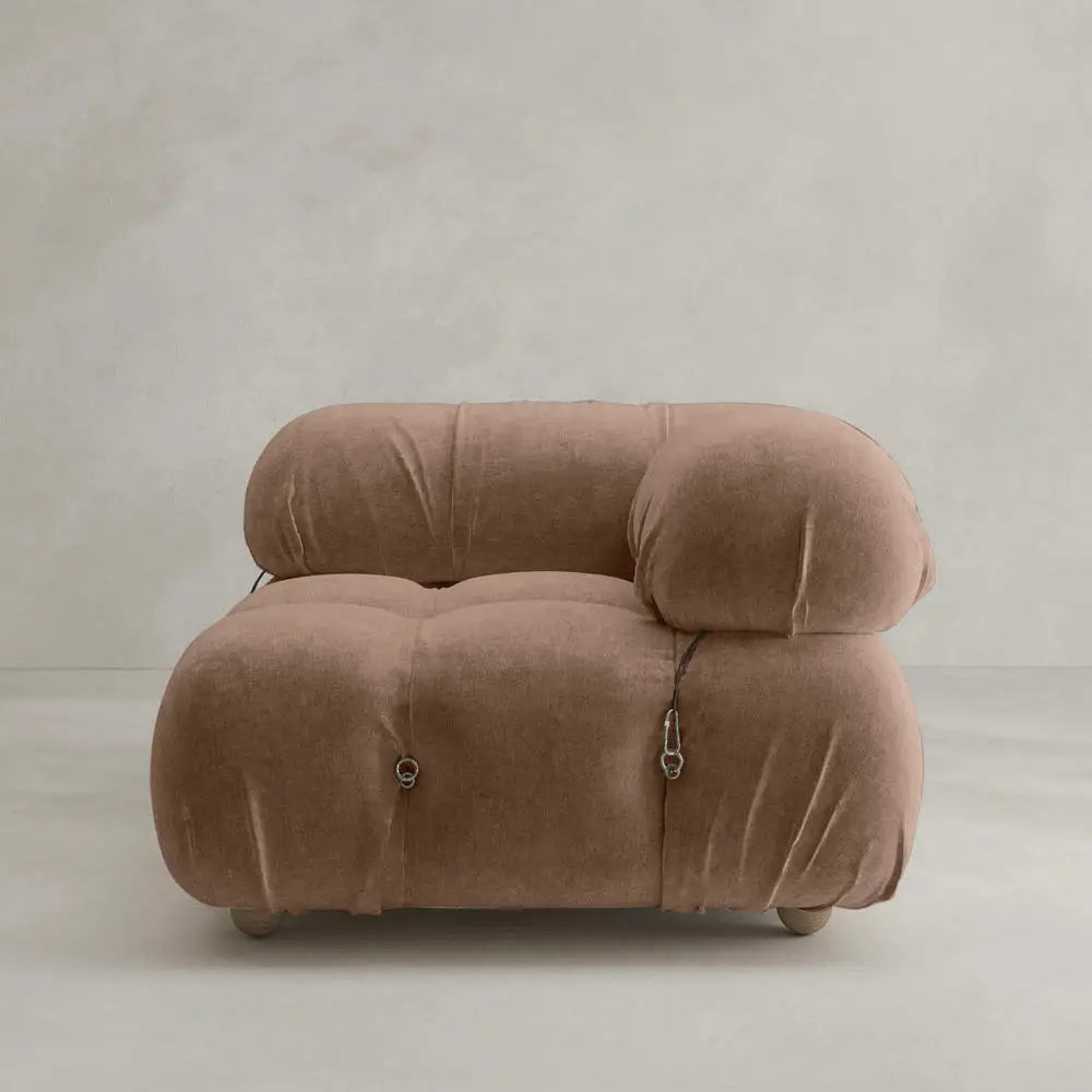 The Belmont Sofa Left Armrest features plush, marshmallow-like curves and overstuffed cushions in soft brown fabric, set against a simple light beige wall and floor background.