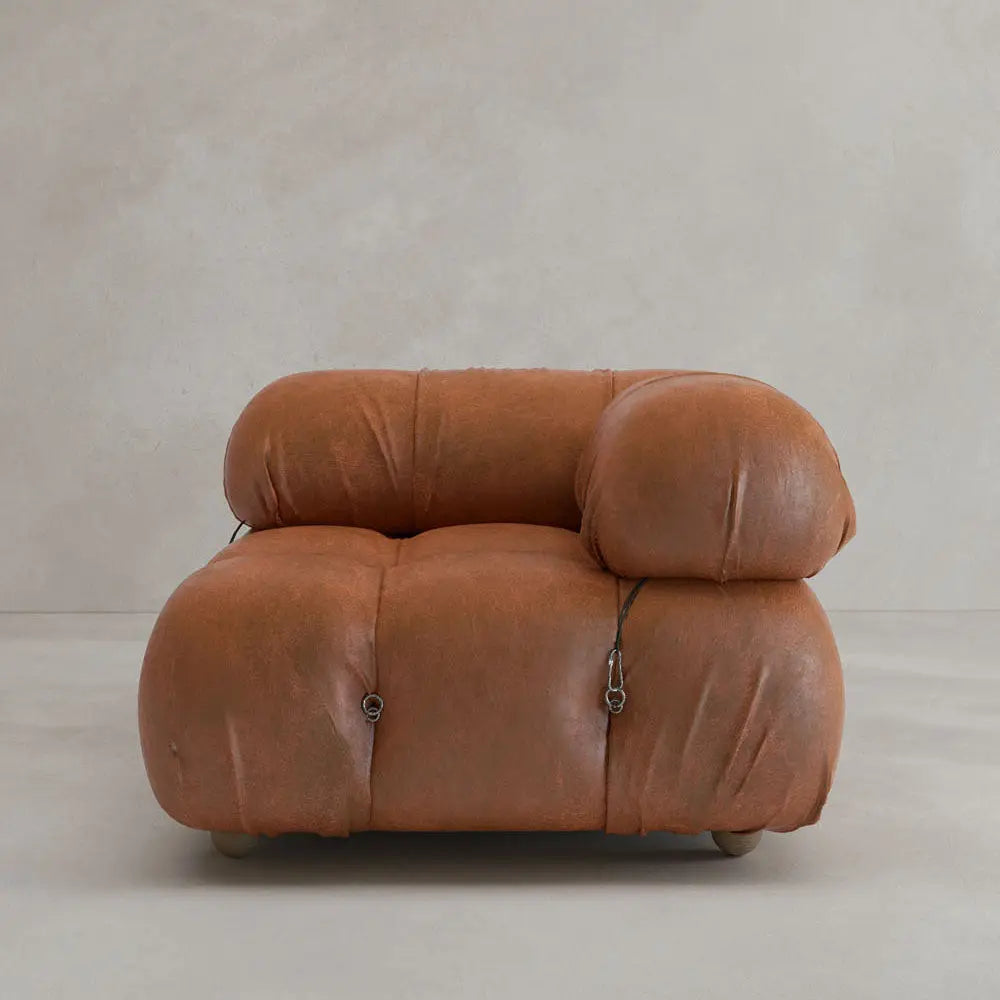 The Belmont Sofa Left Armrest features plush brown leather upholstery, soft rounded edges, tufted details, and visible fasteners. This iconic classic sits on small legs against a plain, light-colored background.