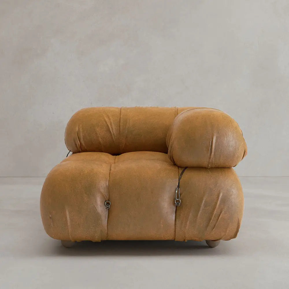 The Belmont Sofa Left Armrest features tan upholstery, overstuffed marshmallow curves, and iconic black straps, creating a classic look against a plain beige background.