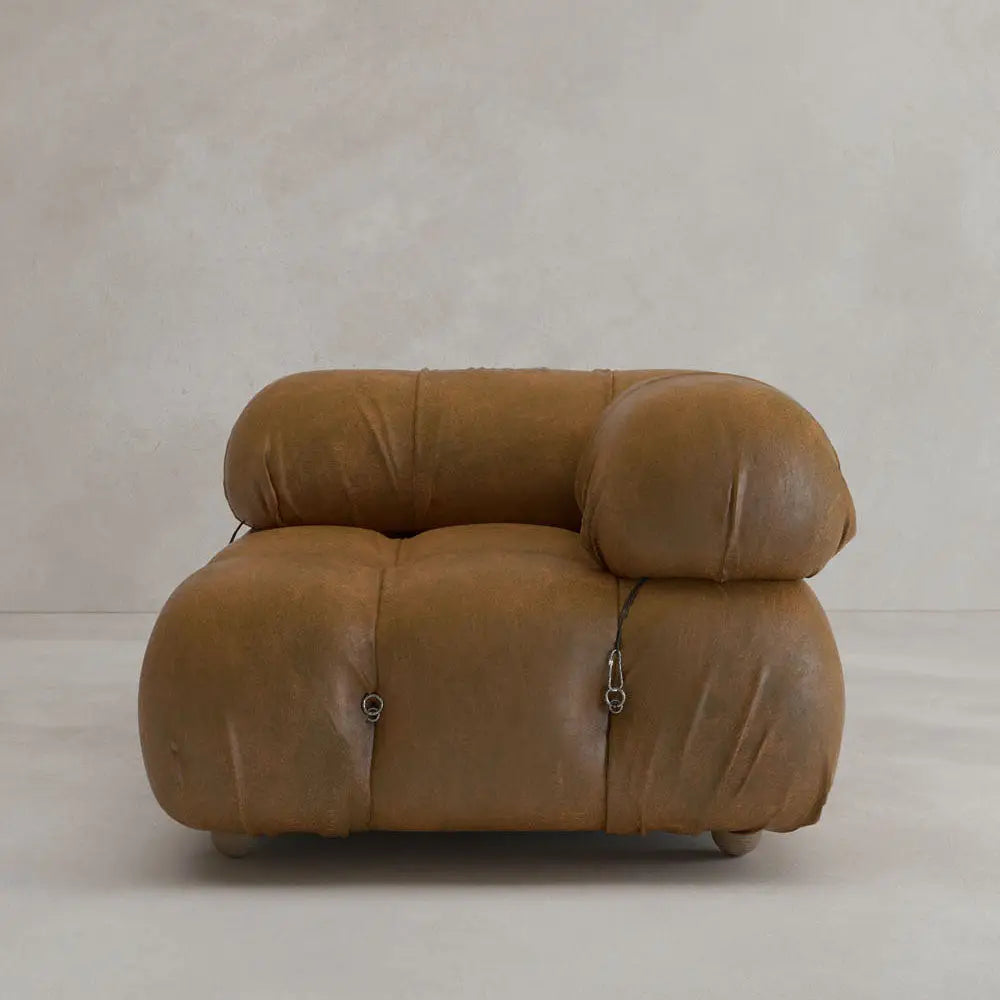 The Belmont Sofa Left Armrest features plush, oversized brown leather with marshmallow-like curves and visible tufted details, set against a plain light beige background.