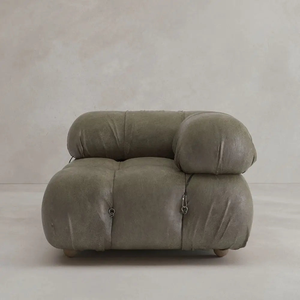 The Belmont Sofa Left Armrest features plush, olive-green upholstery and marshmallow-like curves. Its iconic oversized design includes rounded, tufted details, visible seams, small metal accents, and sits against a light wall.