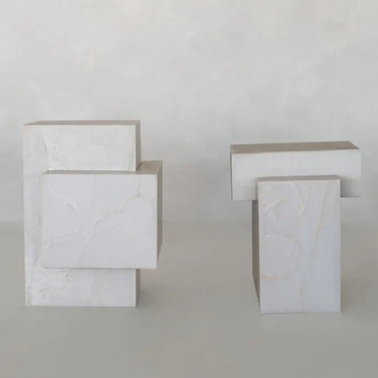 The Bianca Plinth Set features two geometric sculptures of intersecting rectangular and square blocks, crafted from white onyx plinths with subtle veining for a modern, elegant look against a neutral backdrop.