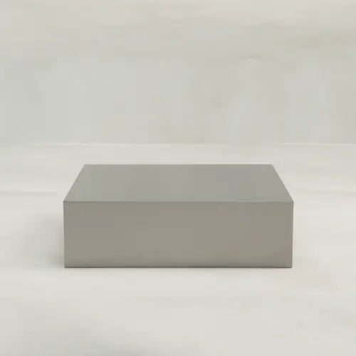 The Forge Steel Large Square Plinth, featuring a brushed metal finish and smooth edges, sits on a light surface, highlighting its modern design against a plain background.