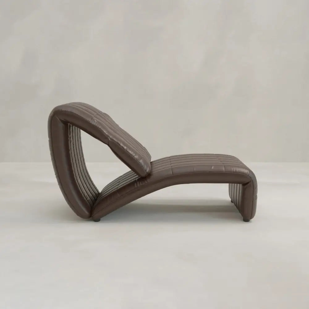 The Hillier Chair, crafted in premium vintage leather, features a contoured wave-like shape and elegant reclining design, shown in brown on a light floor with a neutral textured background.