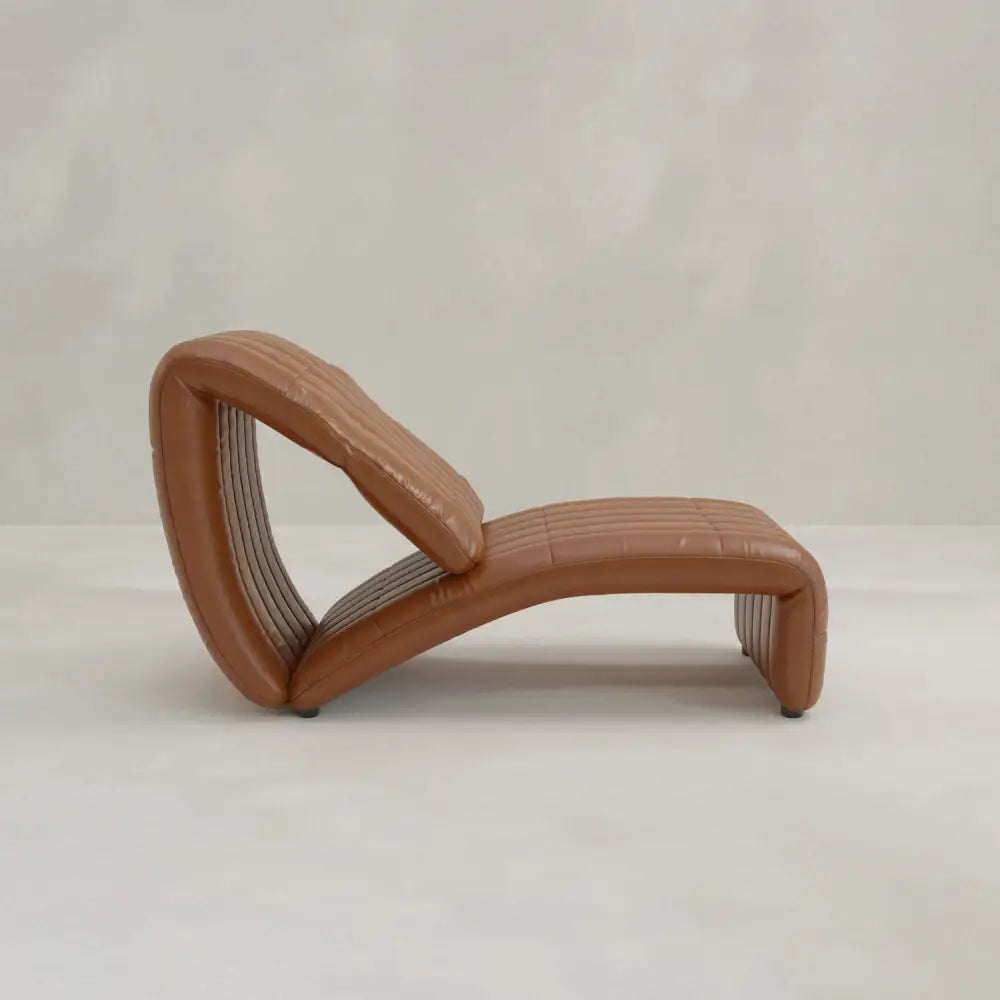 The Hillier Chair, crafted from premium vintage leather, showcases a modern, wave-inspired curved design with reclining features. It rests on a light-textured floor set against a simple, pale background.