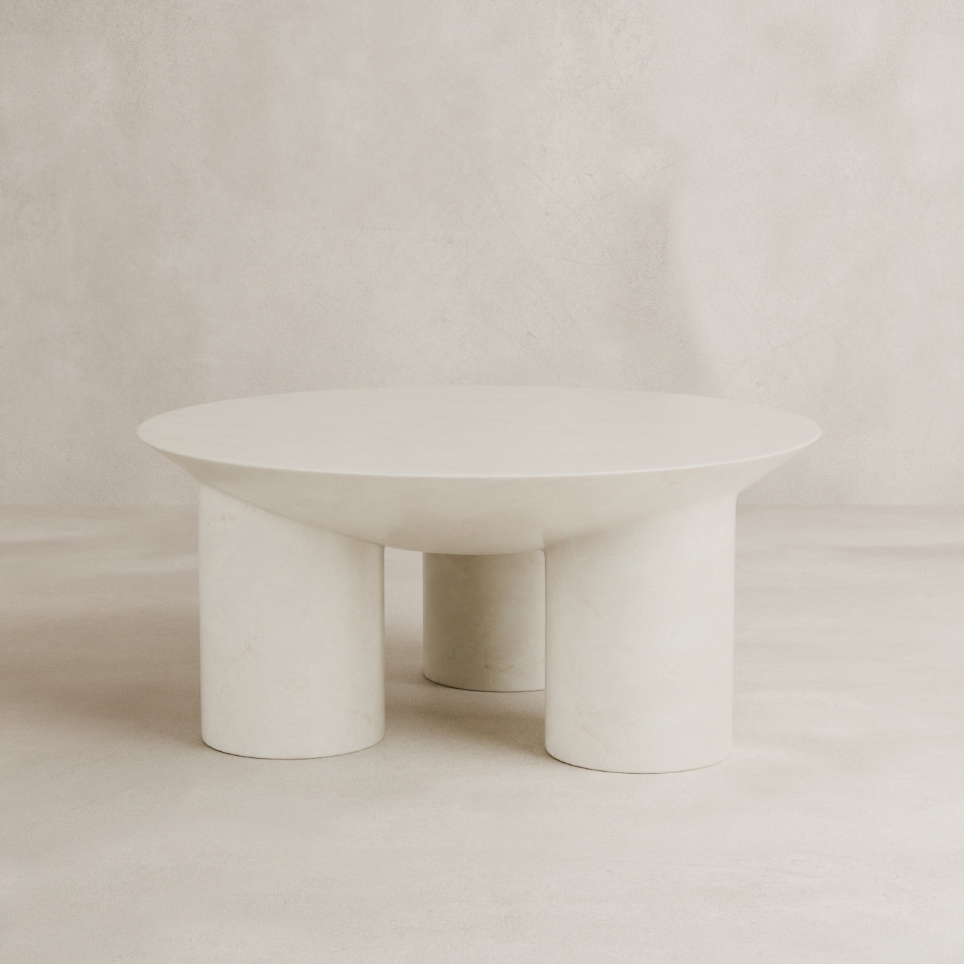 The Luna Coffee Table showcases modern minimalist elegance with thick tubular legs and a smooth off-white fiberglass finish, complemented by a neutral, textured backdrop.