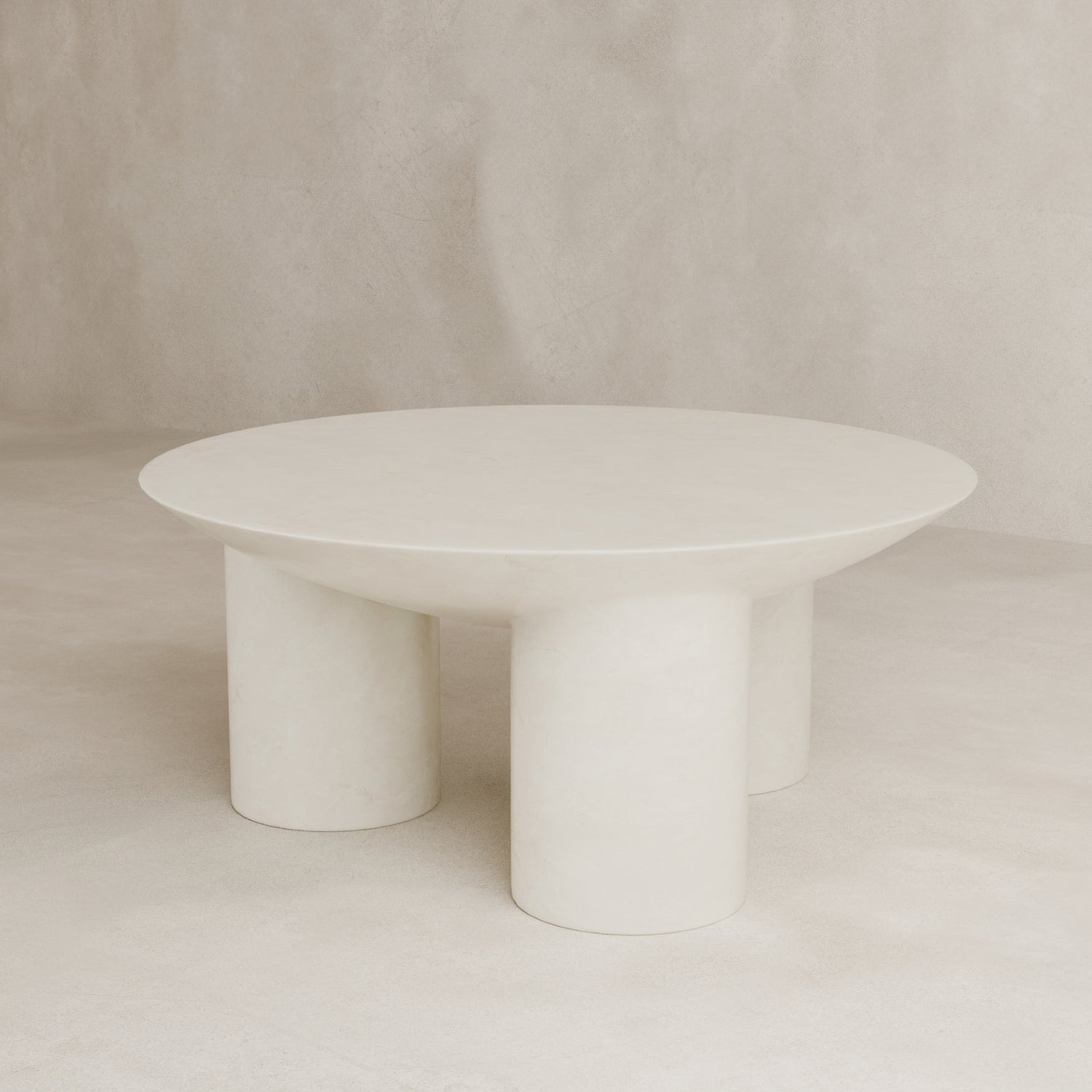 The Luna Coffee Table is a minimalist, round fiberglass piece with a smooth surface and three thick tubular legs, shown on an off-white background for modern elegance.