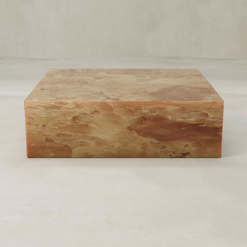 The Ambeline Onyx Coffee Table XL features a square, low-profile design in polished brown and beige marble, adding organic elegance with its smooth, sculptural form against a neutral background.
