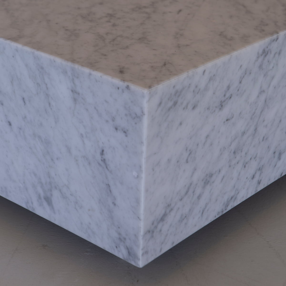 Close-up of the Aurora Marble Plinth, a polished rectangular block with gray veining and clean edges, resting on a flat, light-colored floor.