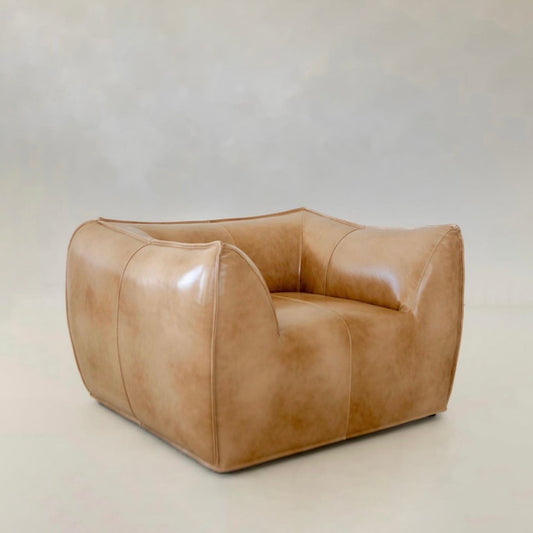 The Bambon Armchair features a modern, oversized boxy silhouette with organic lines and smooth tan leather upholstery, showcased against a plain light background.