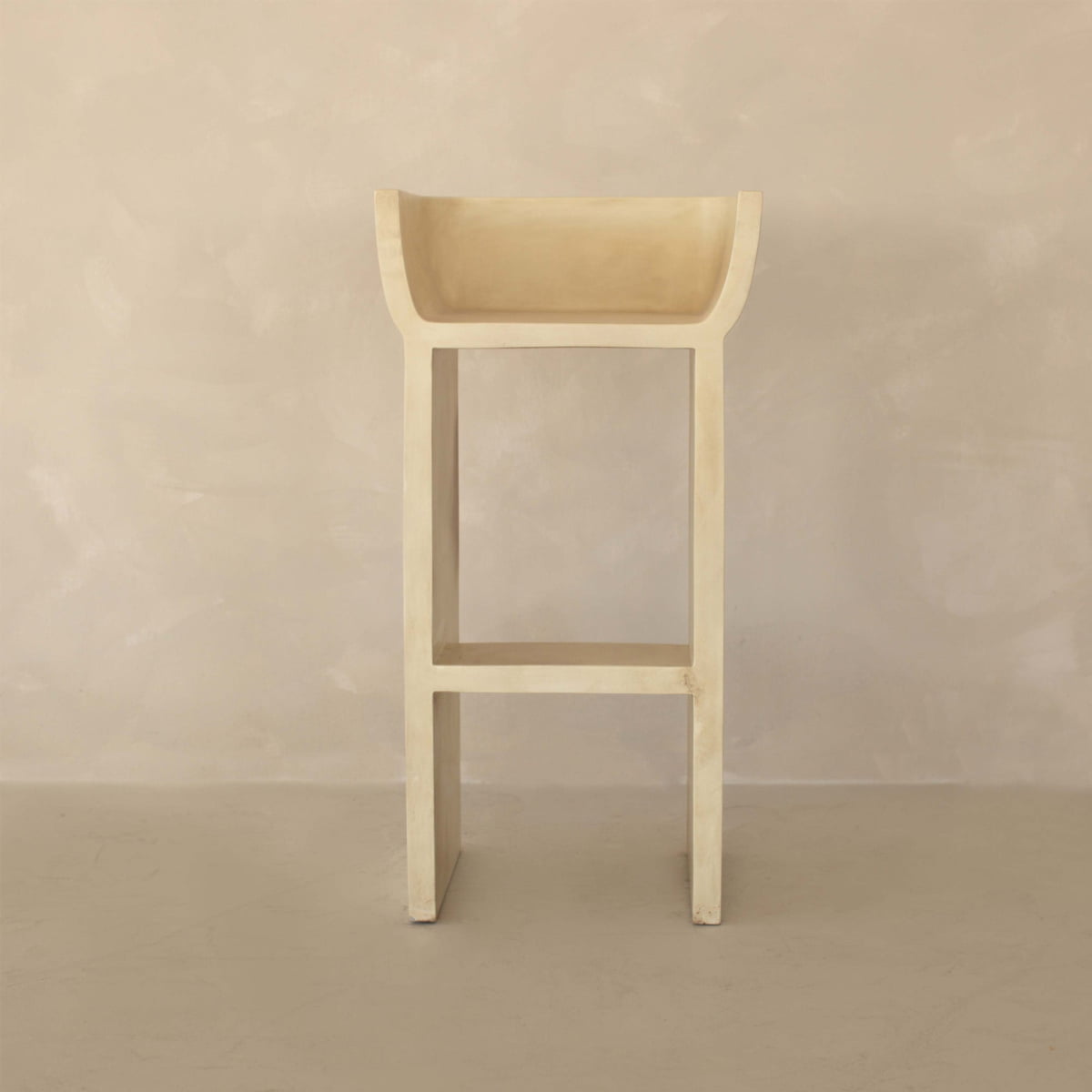The Barbican Stool, tall and minimalist in beige with clean lines and a rectangular seat, adds urban elegance to the space, complementing the light beige textured wall and floor.