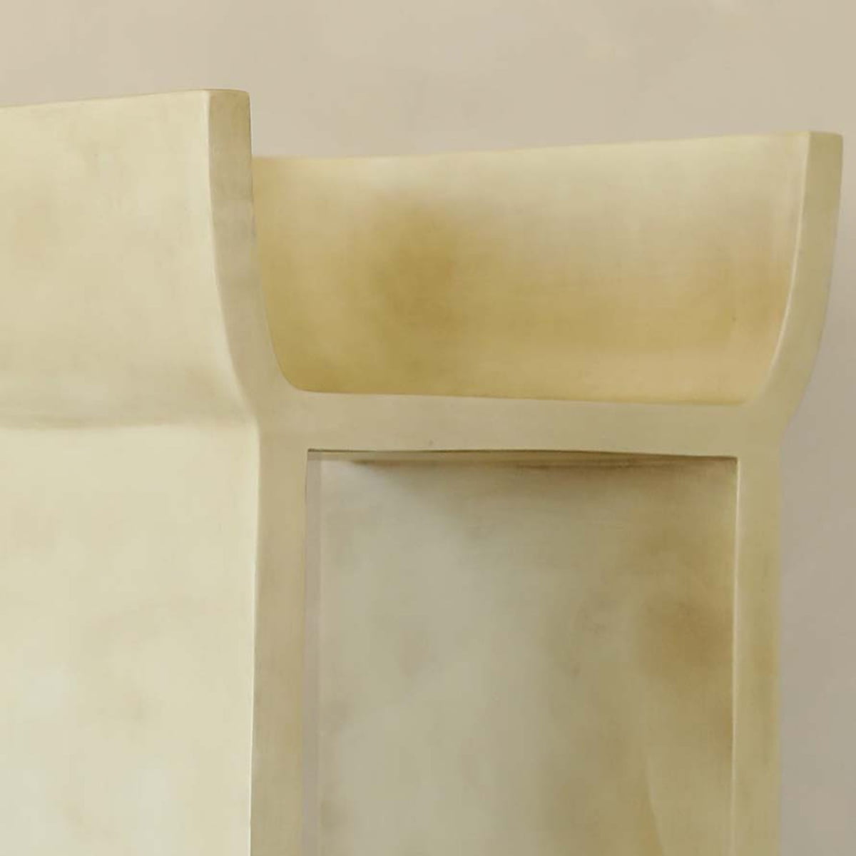 Close-up of the Barbican Stool’s modern, minimalist beige surface with smooth, curved, and rectangular shapes that recall mid-century Brutalism—adding depth and shadow for an urban elegance against a plain backdrop.