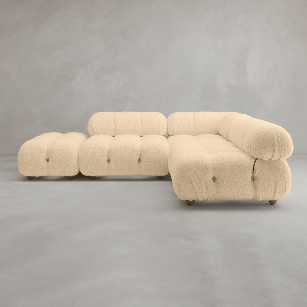 The Belmont Sofa Combination B is a modern modular cream cloud sofa with plush tufted cushions, rounded edges, and metal button accents, set on a smooth gray floor against a light gray wall for an iconic classic look.