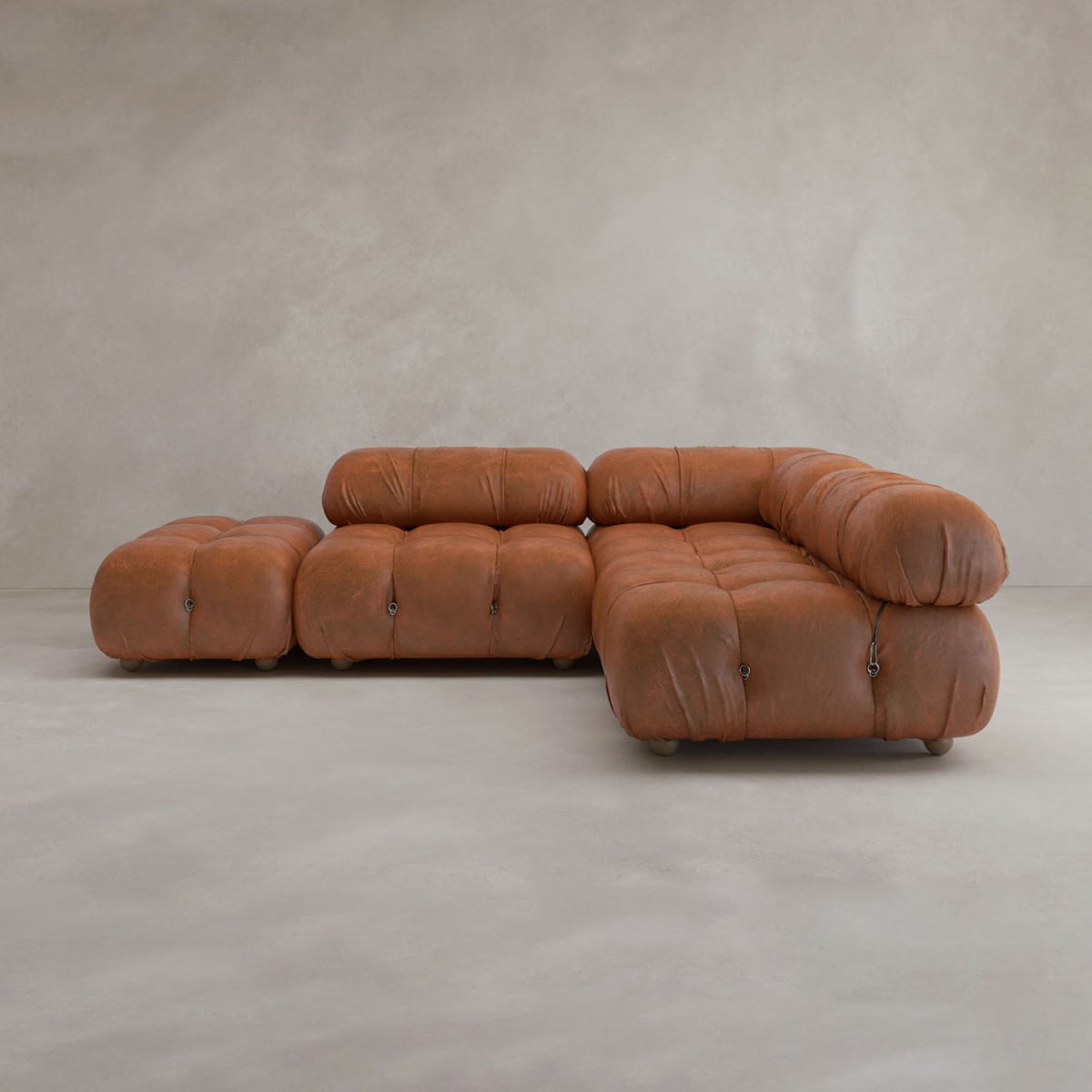 The Belmont Sofa Combination B, a modular brown leather sectional with tufted cushions and rounded plush shapes, sits on a light gray floor against a textured beige wall.