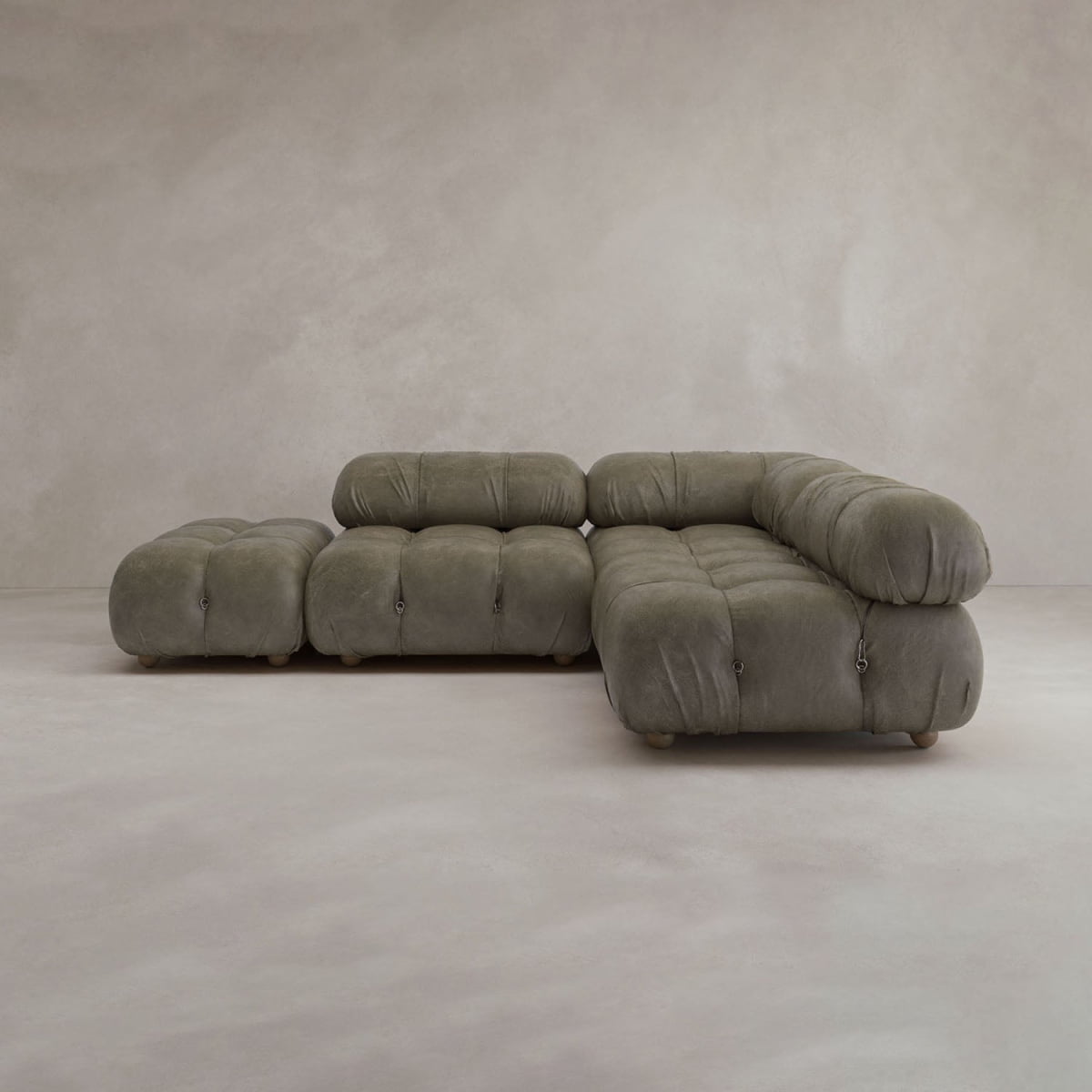 The Belmont Sofa Combination B features plush, tufted olive-green upholstery in a modern, modular design. It sits on a smooth, light floor against a plain, neutral wall, evoking an iconic classic style.
