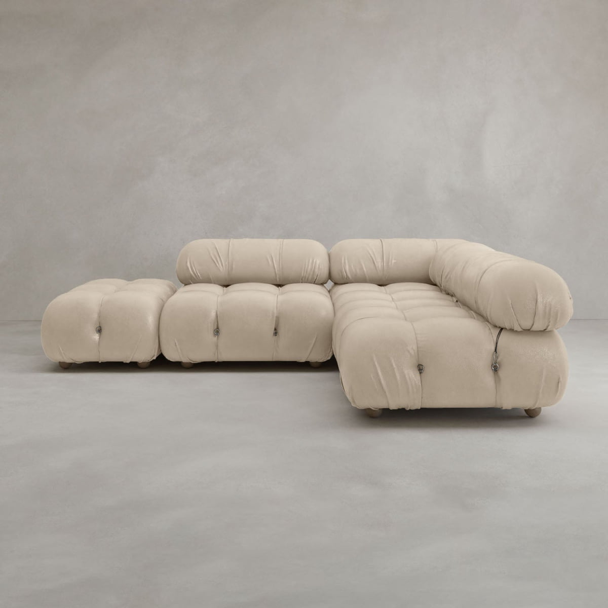 The Belmont Sofa Combination B, a modern beige modular sofa with tufted cushions and rounded edges, sits in an empty room with light gray walls and flooring.