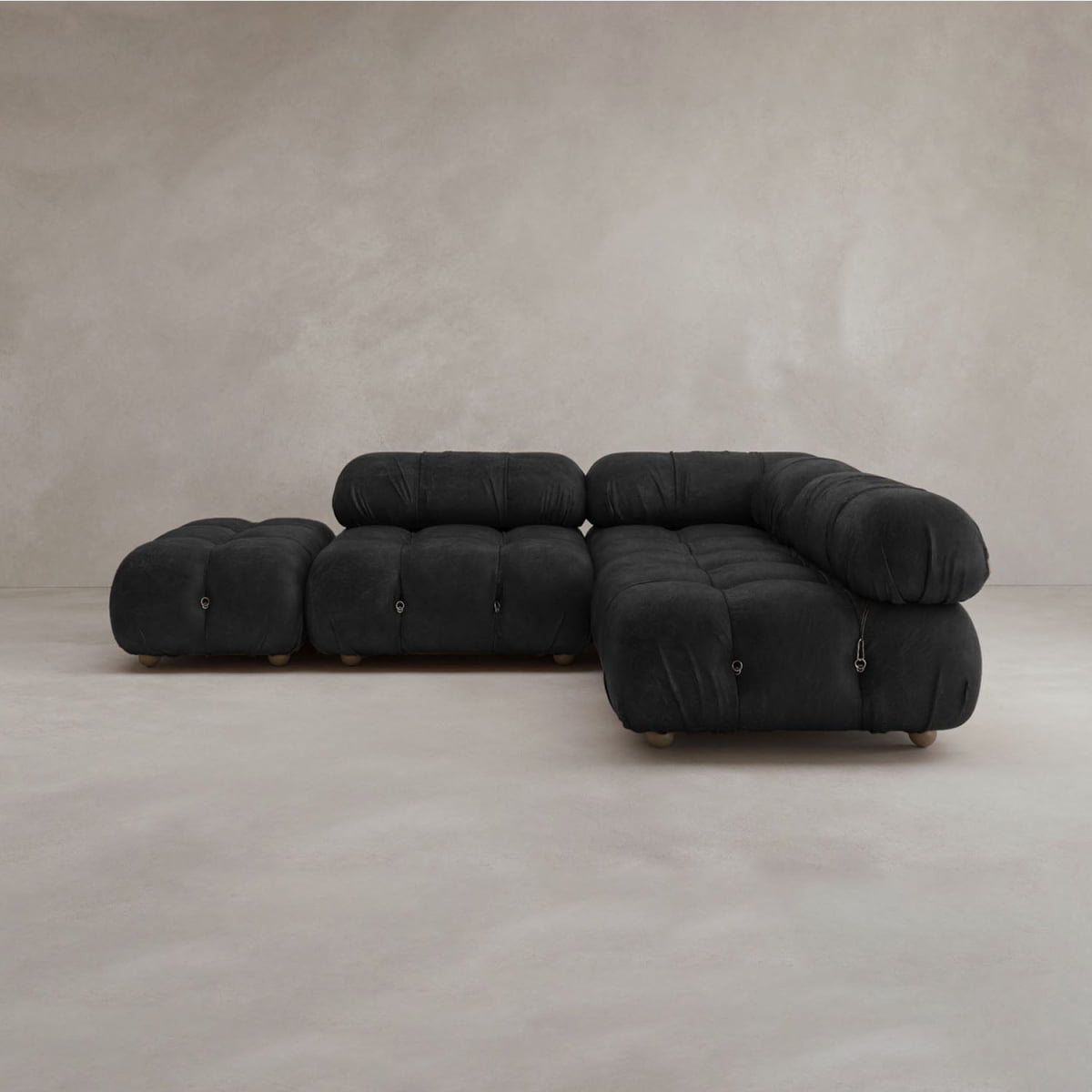 The Belmont Sofa Combination B is a modern black modular sofa with rounded tufted cushions and an attached ottoman, placed in a neutral, minimalist setting.