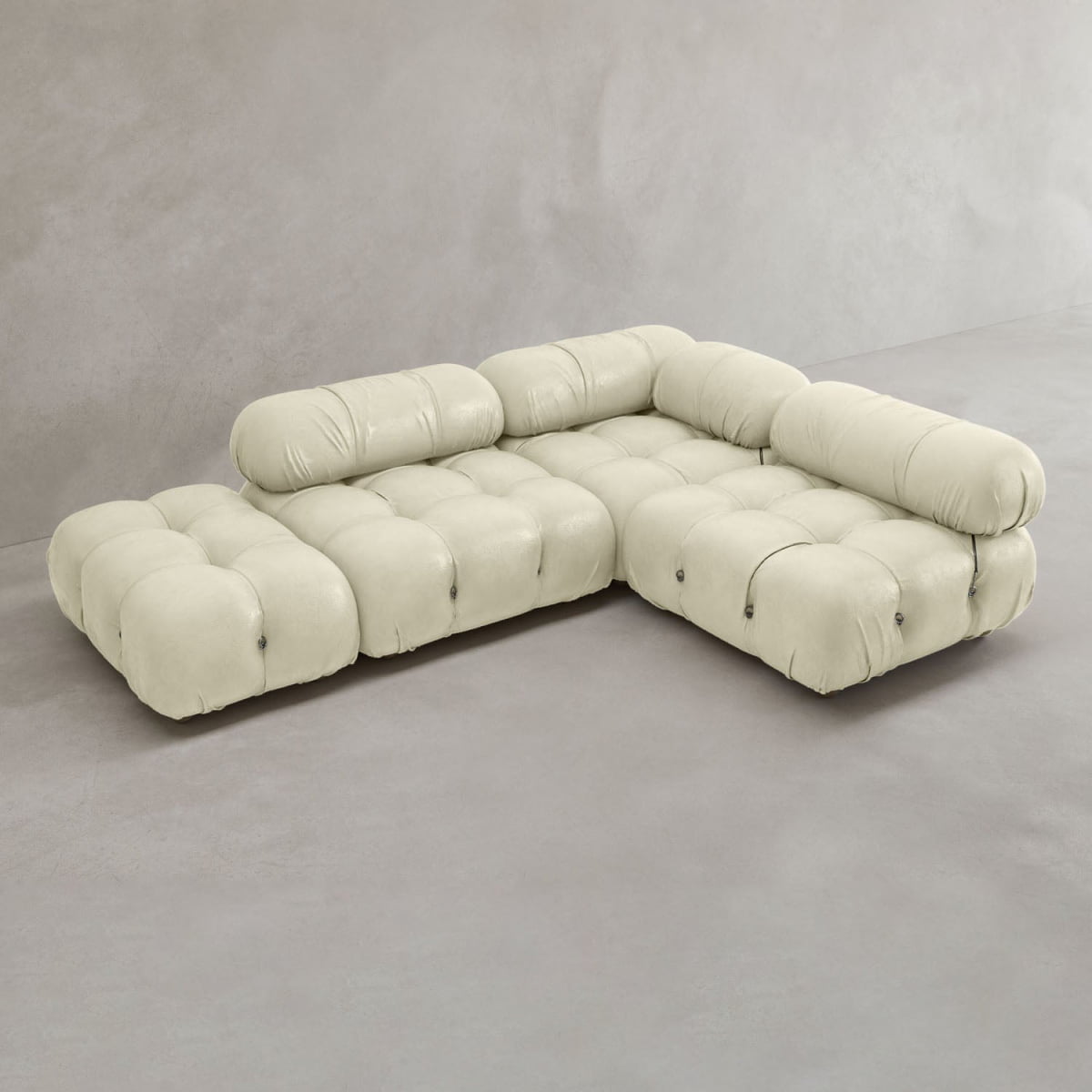 The Belmont Sofa Combination B, a modern light beige modular sofa with tufted cushions and low backrests in an L-shape, is arranged in a minimalistic room featuring gray floors and walls.
