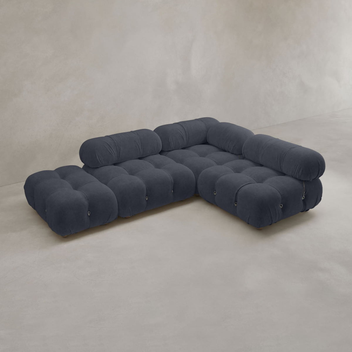 The Belmont Sofa Combination B is a modern, dark gray modular sofa featuring rounded, tufted cushions and low backs, set against a plain light wall and floor for a classic-inspired look.
