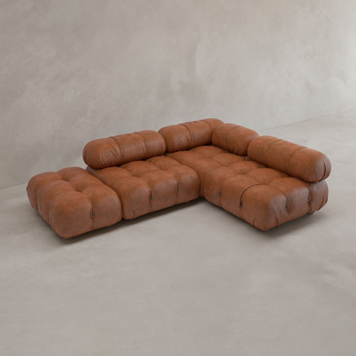 The Belmont Sofa Combination B features tufted brown leather cushions and rounded edges, inspired by iconic classics. It is displayed on a light gray floor against a beige wall.