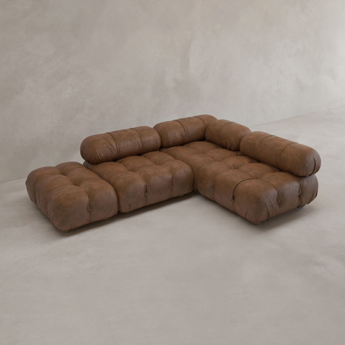 The Belmont Sofa Combination B, a modular brown leather sectional with tufted cushions and rounded edges inspired by the classic cloud sofa, sits on a light gray concrete floor against a plain beige wall.