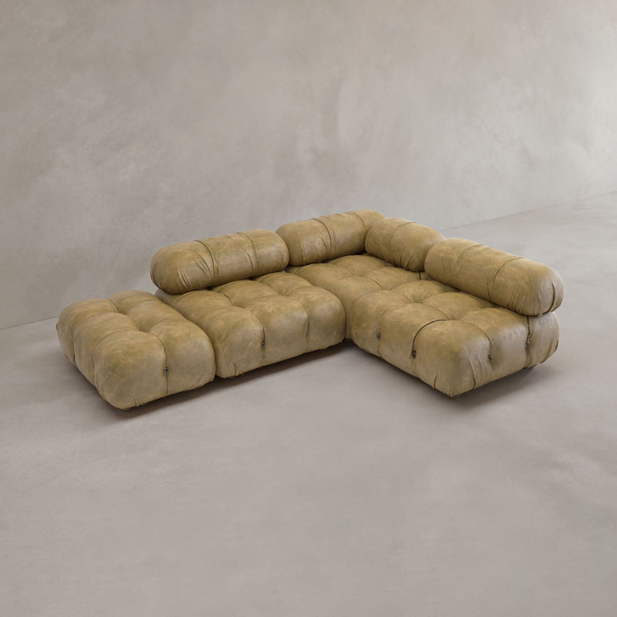 The Belmont Sofa Combination B, a low-profile L-shaped modular sofa with tufted tan leather upholstery, is placed in an empty room with plain light-colored floors and walls.