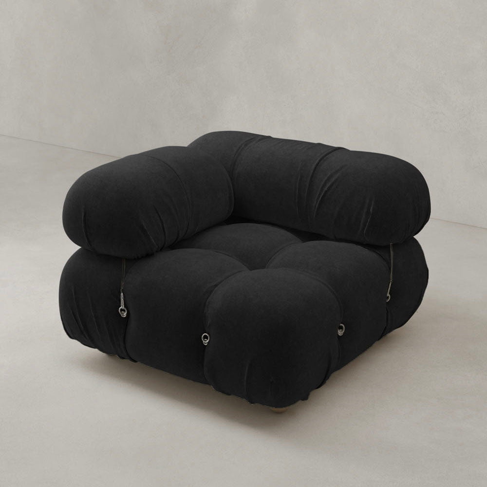 The Belmont Sofa Right Armrest, with its modern black tufted design and plush, rounded cushions, adds iconic classic style to your dream space when placed against a light beige wall and floor.