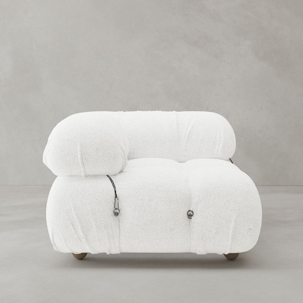 The Belmont Sofa Right Armrest features plush, textured white fabric with visible black cord accents and a modern low-profile design, adding iconic classic style to any setting with its sleek look against gray concrete walls and floors.