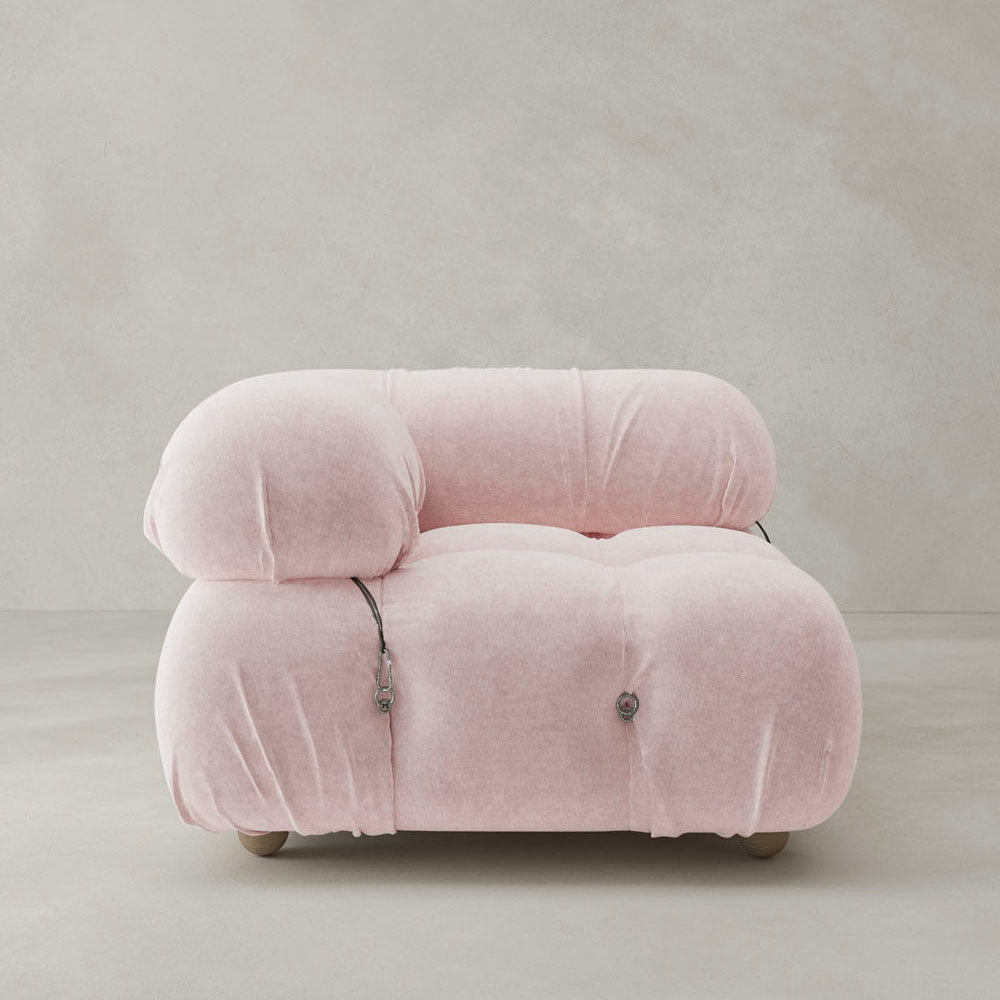 The Belmont Sofa Right Armrest features plush pale pink upholstery, rounded overstuffed cushions, and visible metal buckle accents on the sides, exemplifying modular design against a plain light gray background.