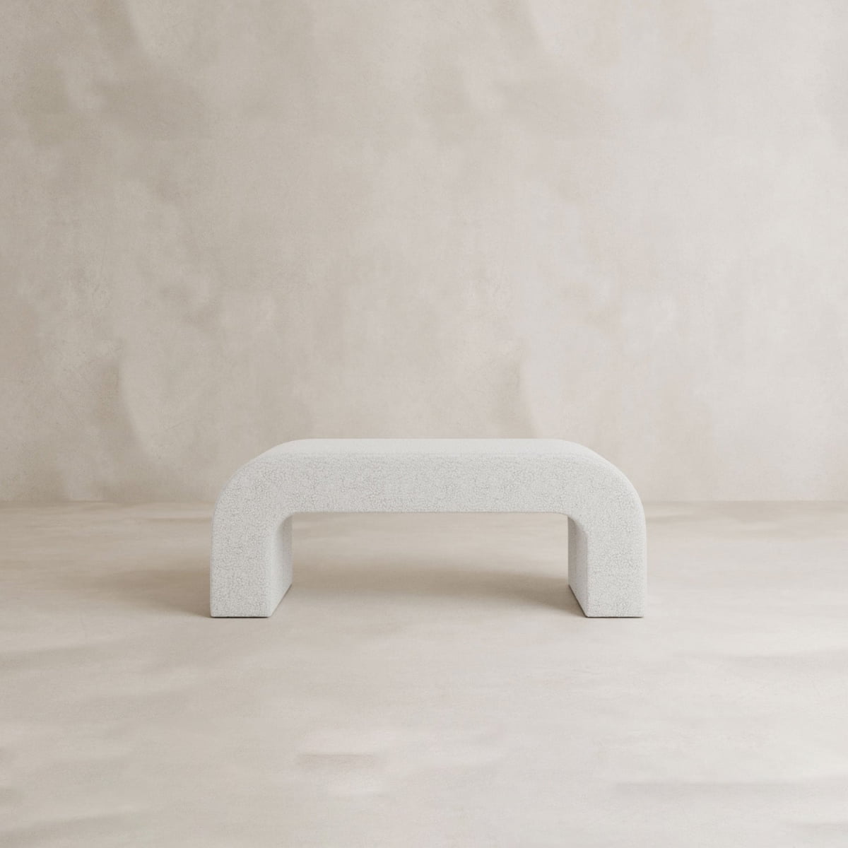 The Beverly Bench, a minimalist white boucle seat with an arched base, is set against a light beige textured background, lending modern elegance to this simple, contemporary space.