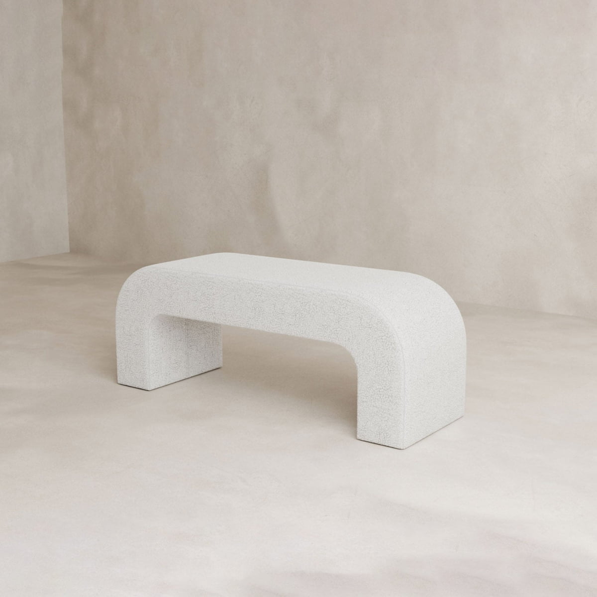 The Beverly Bench, a modern and minimalist white boucle bench with curved edges and smooth surface, adds elegant style to any interior when placed against a neutral, light-colored background.