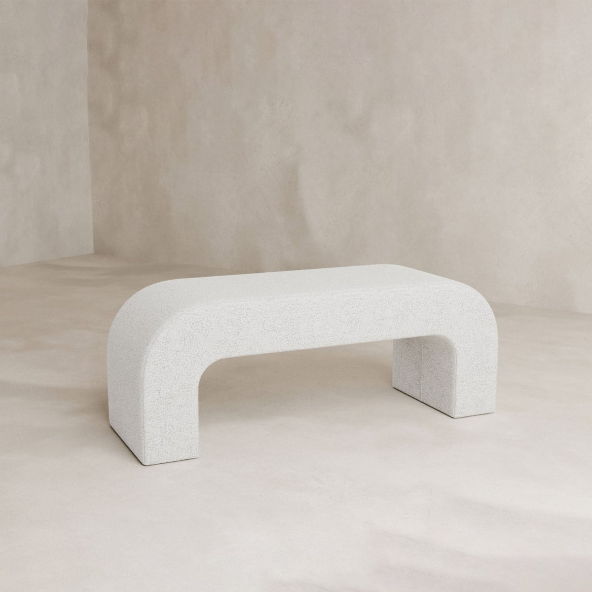 The Beverly Bench, featuring a minimalist white boucle and rounded edges with a U-shaped design, adds modern elegance to your space as it sits on a light beige floor against a matching neutral wall.