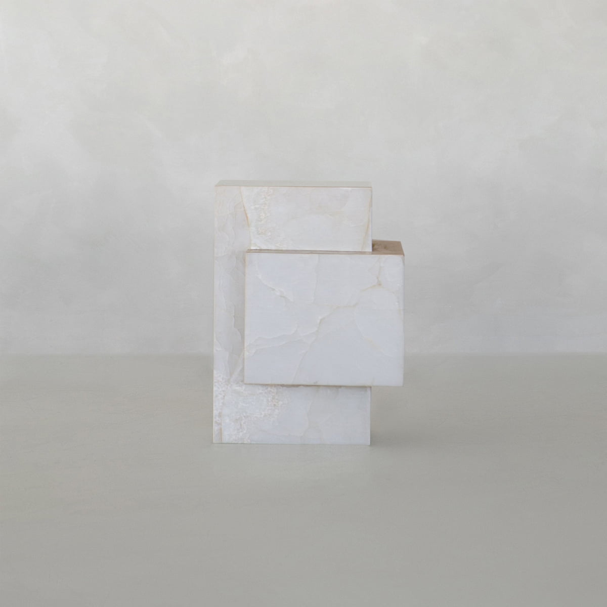 The Bianca Tall is a minimalist white onyx sculpture with visible veins, featuring two rectangular plinths interlocked at a right angle against a neutral, textured background.