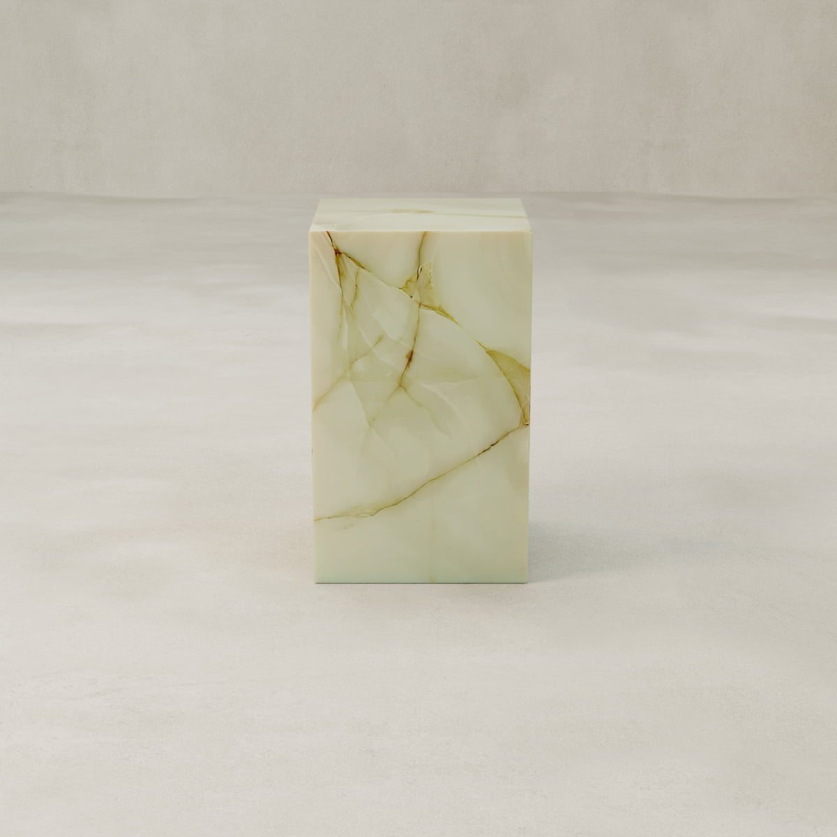The Blanchaire Onyx Plinth - Tall features a luminous finish and delicate veining in pale green and gold, set on a smooth light surface against a neutral backdrop.