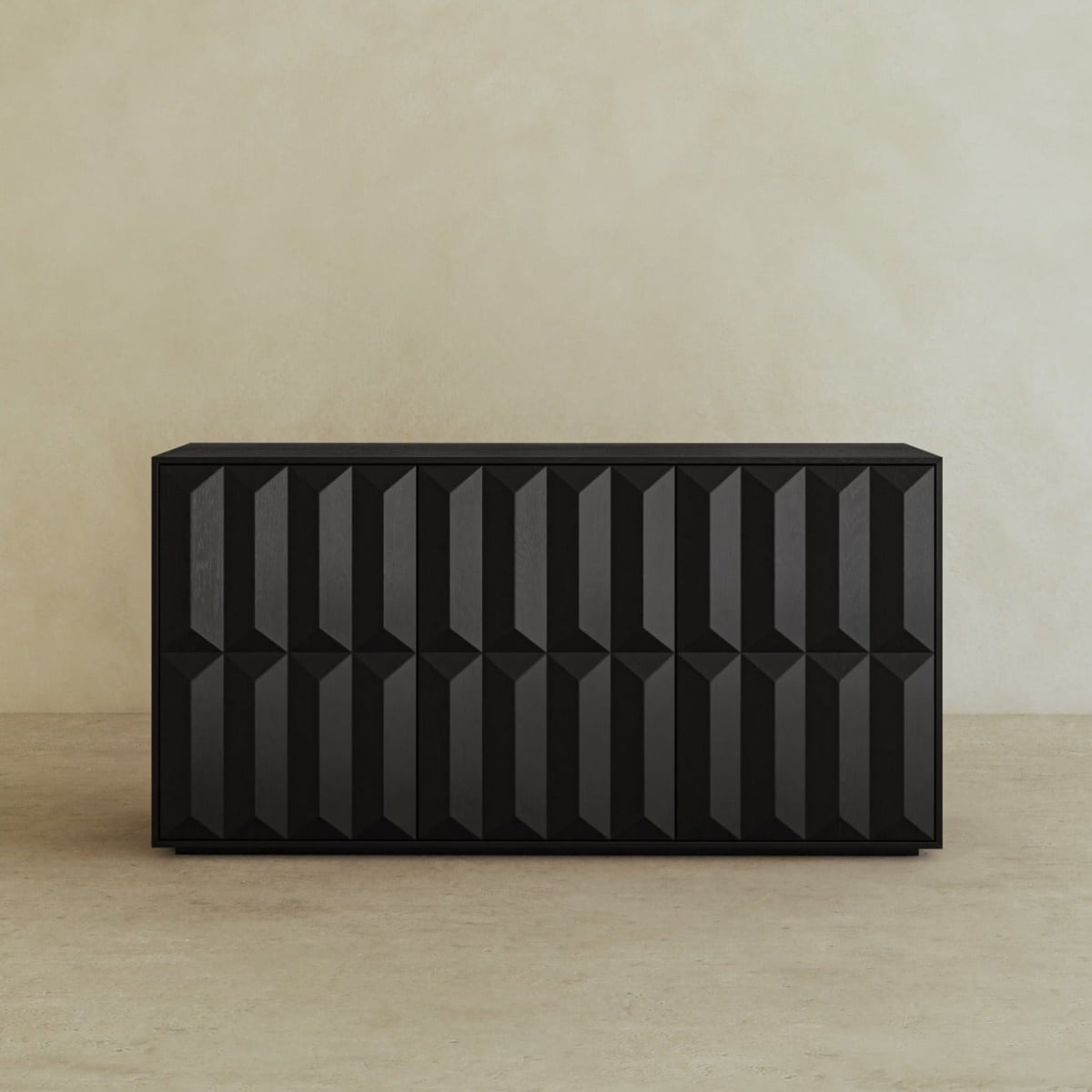 The Braemar Console Large, designed by Anthony Newman, features a modern black finish with a geometric textured front, standing out against a simple beige wall and floor for an avant-garde look.