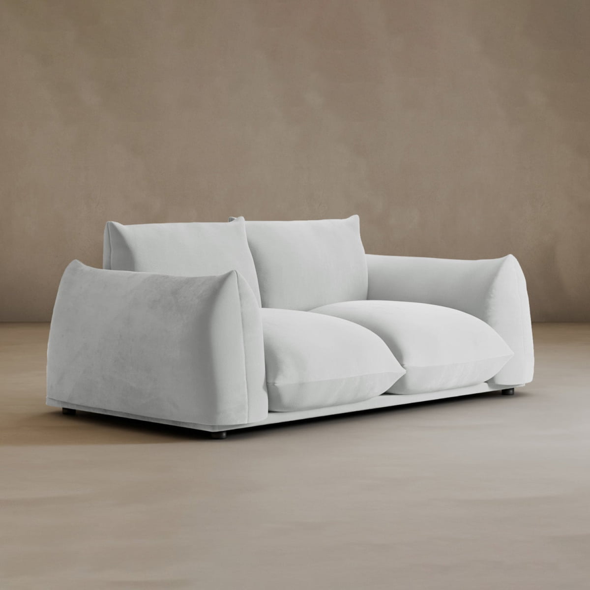 The Calypso Loveseat, featuring plush cushions and modern elegance, is placed on a light floor against a plain beige wall in a minimalist setting.