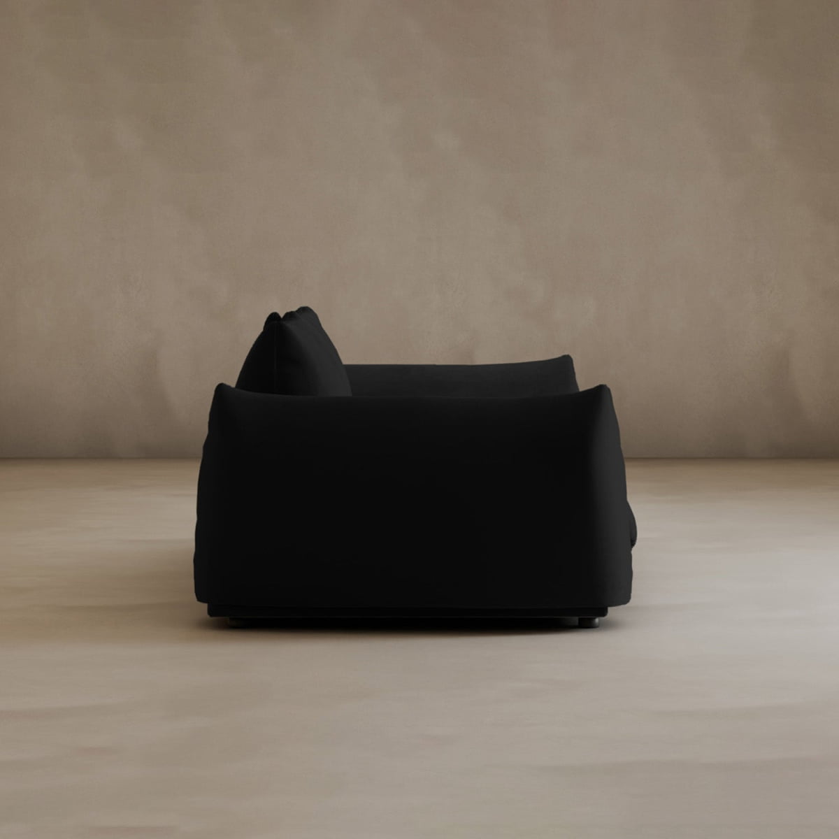 A modern black Calypso Loveseat viewed from the side, set against a plain beige wall and floor with minimalistic, neutral-toned decor, exuding contemporary elegance.