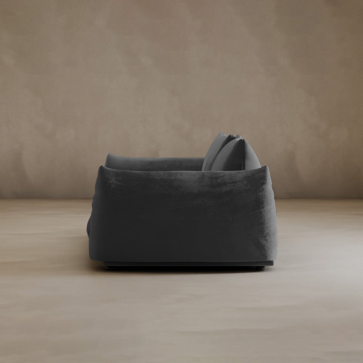 A modern, dark gray Calypso Loveseat with plush cushions is displayed in profile against a neutral beige wall and floor, creating a minimalistic and cozy atmosphere that exudes modern elegance.
