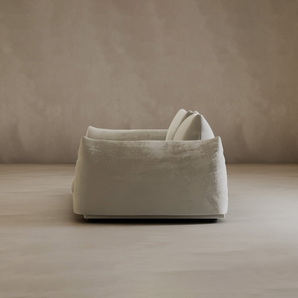 A modern, plush Calypso Loveseat with two large cushions exudes sleek elegance, viewed from the side on a smooth beige floor against a textured light brown wall.