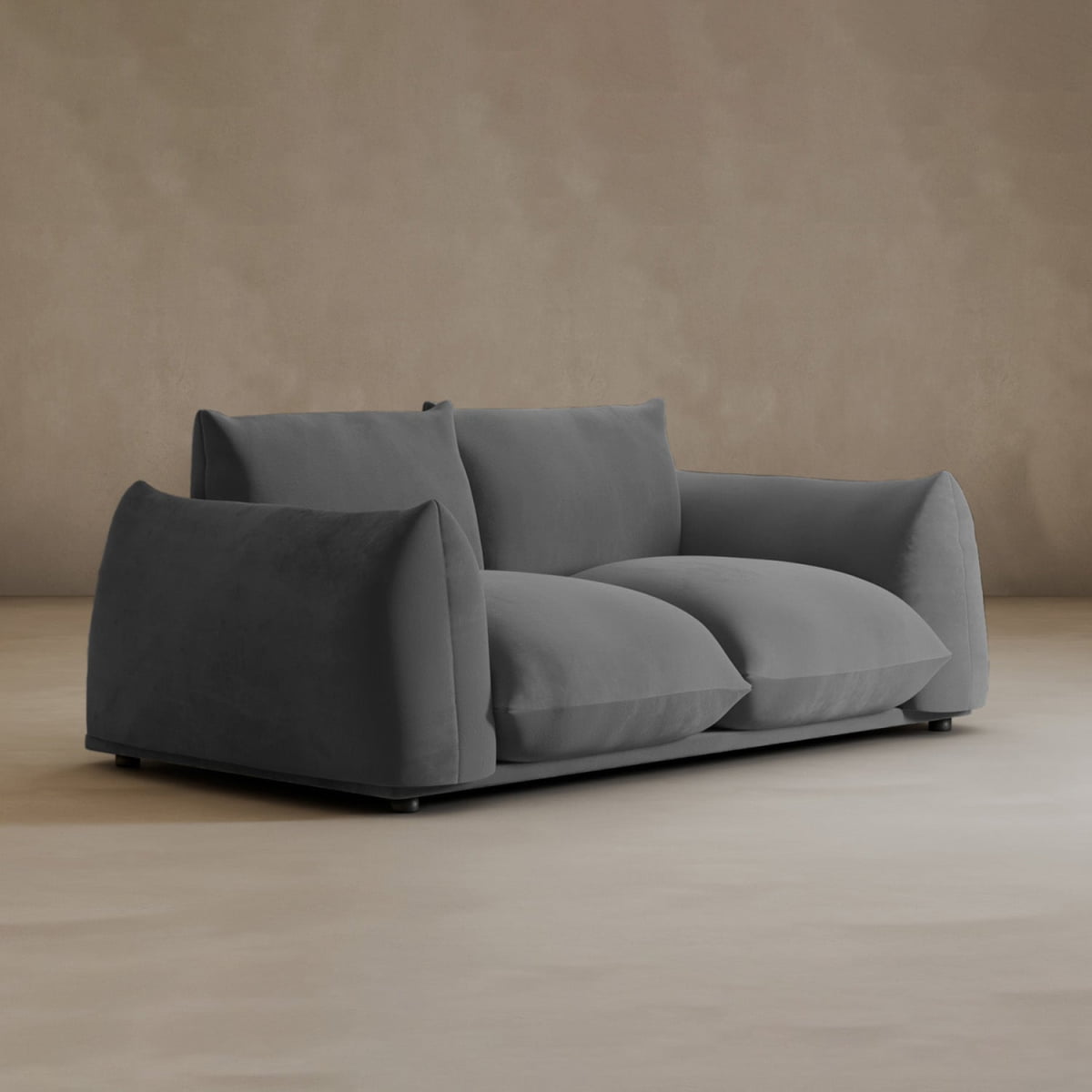 The Calypso Loveseat in dark gray, featuring plush cushions, is displayed on a light beige floor with a matching beige wall for a modern, elegant look.
