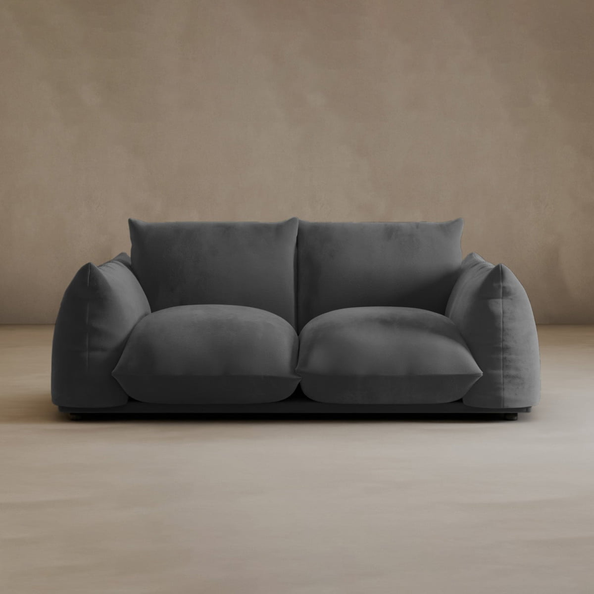 A modern, dark gray Calypso Loveseat with oversized cushions exudes contemporary elegance against a plain beige wall and light floor in a minimalist room.