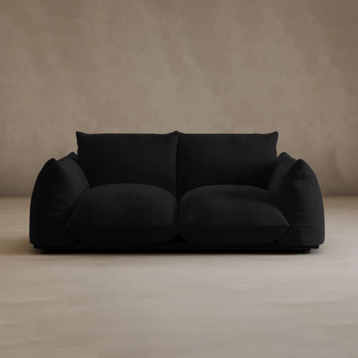 A plush Calypso Loveseat with large, overstuffed cushions sits against a plain beige wall and light floor, bringing modern elegance to the minimalist setting.