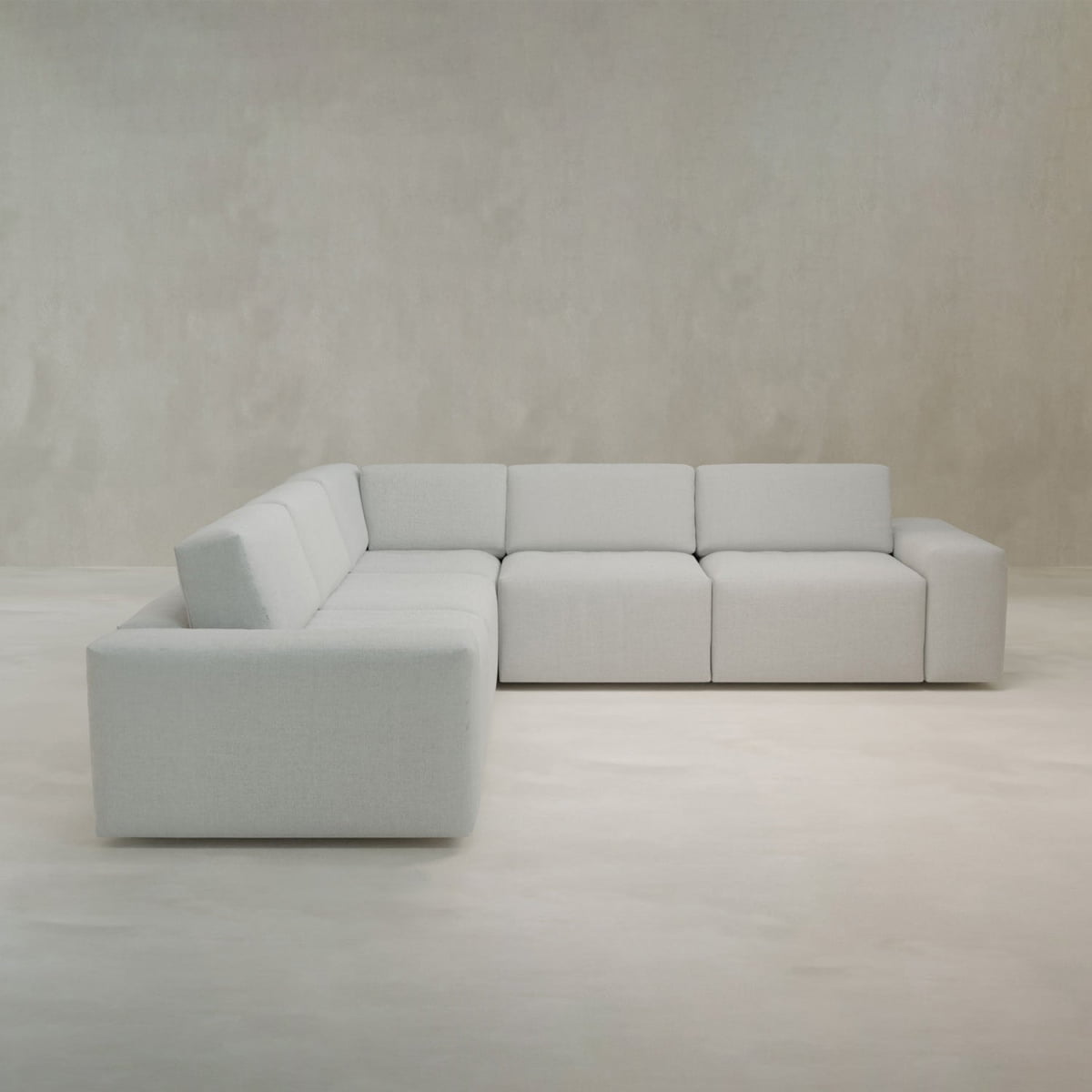 The Canonbury L Shape Sofa features a large, modern design with clean lines and low backs, offering contemporary comfort and customizable seating in a room with light gray walls and flooring.