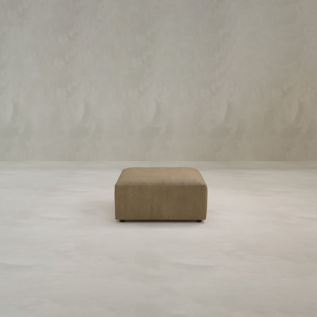 A minimalist room showcases the Canonbury Ottoman, a rectangular brown piece in high-performance fabric, centrally placed on a light-colored floor against a textured beige wall.