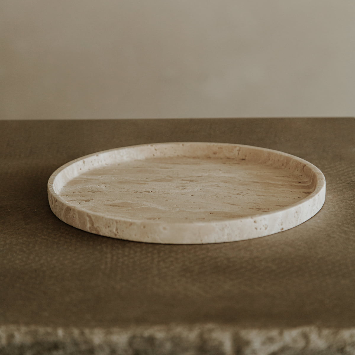 The Cascade Tray in Large, featuring a round and flat design with a slightly raised edge, rests on a textured brown surface, highlighting its natural elegance against a simple neutral background.